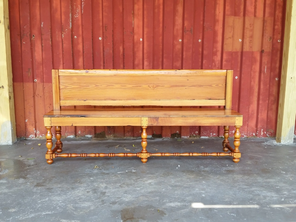 Light brown wooden bench in front of red siding of a building