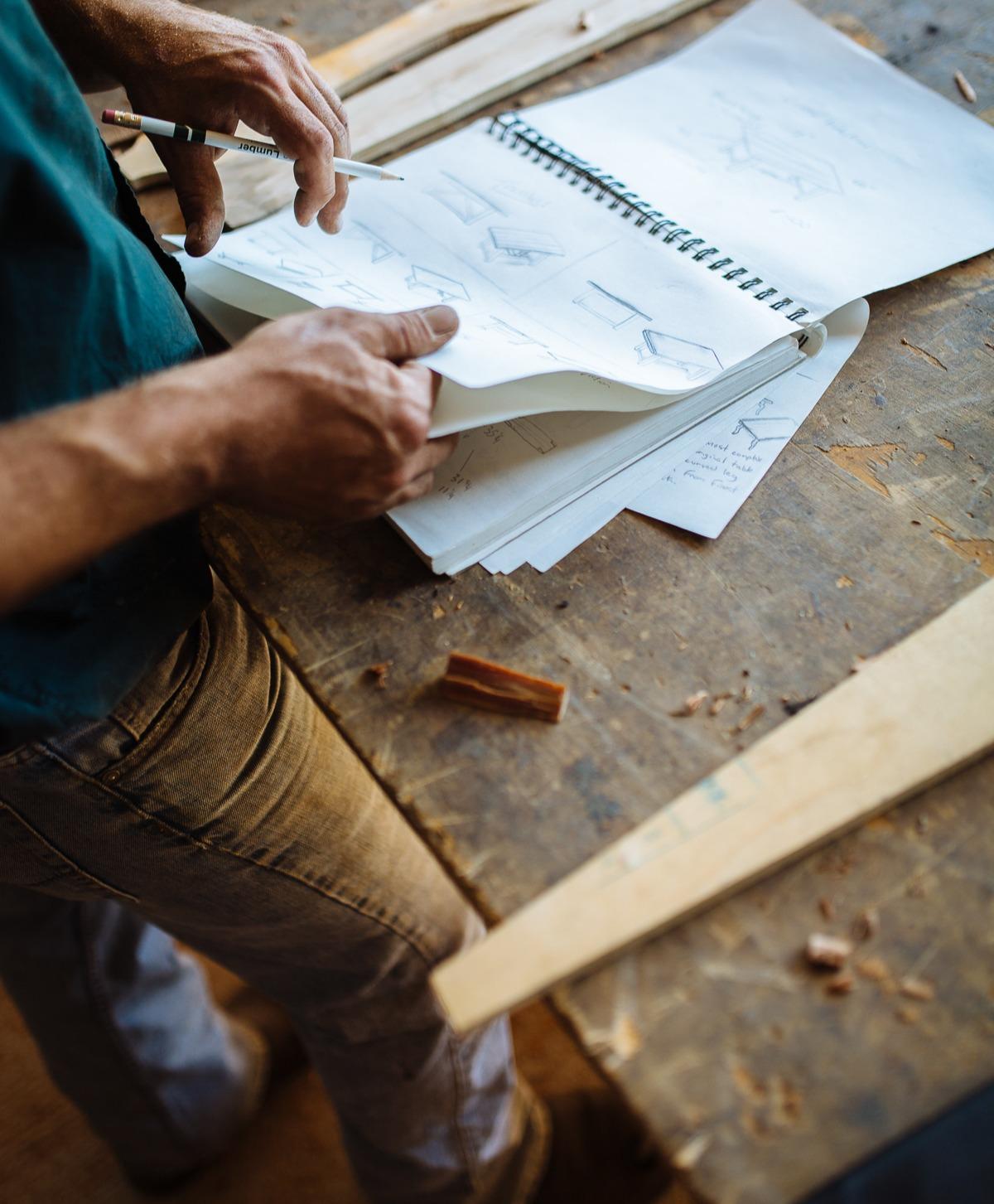 Stephen standing at his workbench examining some custom furniture drawings he has created